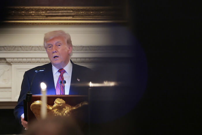 Former President speaking at a podium with candles in foreground, related to January 6 conspiracy theorist Joe Kent appointment.