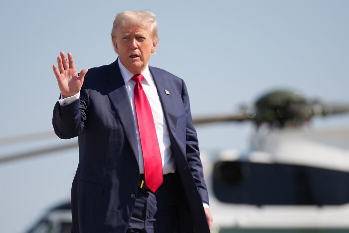 Donald Trump in a suit and red tie, raising his hand, with a helicopter in the background referencing Epstein and Virginia Giuffre.