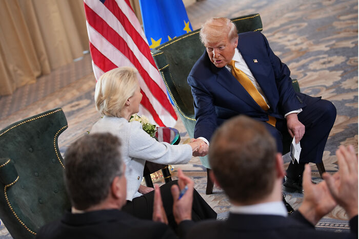 U.S. and EU leaders shaking hands, agreeing on a trade deal with 15% tariffs on most European goods.