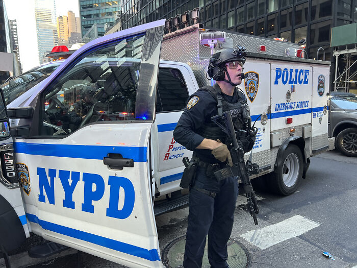 NYPD officer with tactical gear standing by police emergency vehicle during New York shooter incident response.