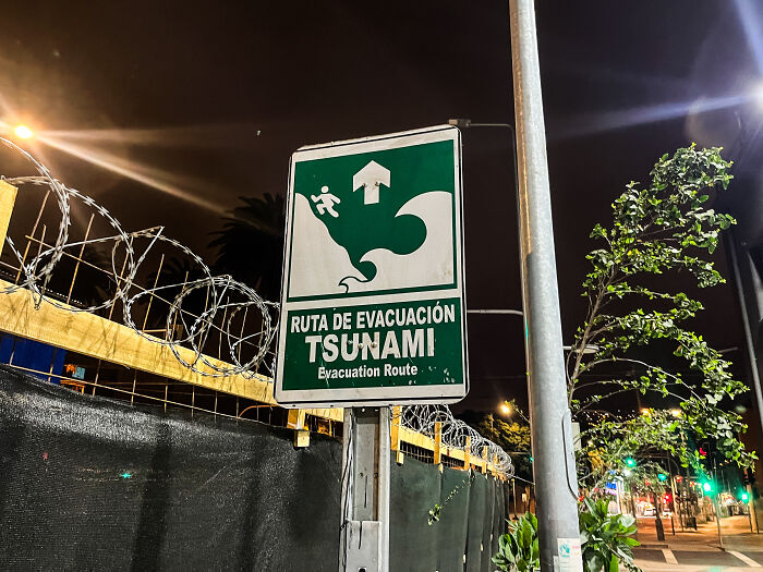Tsunami evacuation route sign at night with barbed wire and streetlights, highlighting tsunami waves strike Hawaii alert.