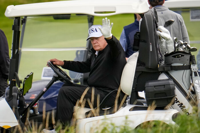 Former President Trump waving from a golf cart at Turnberry, linked to viral golf video and cheating claims.