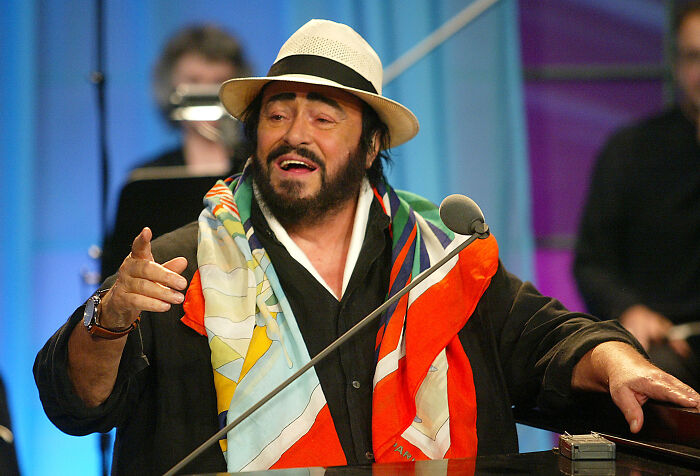 Man speaking passionately at a microphone, wearing a colorful scarf and hat, related to neocon war hawk and Trump tears.