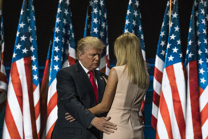 Donald Trump and a woman embrace on stage with multiple American flags in the background related to Trump&rsquo;s dating remark controversy.