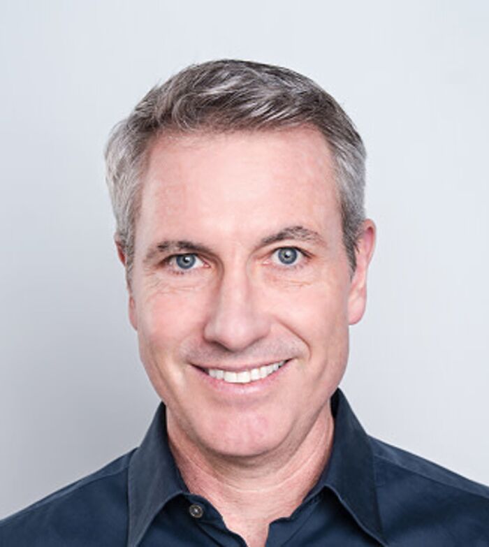 Smiling middle-aged man with gray hair and blue eyes wearing a dark shirt, representing Coldplay CEO privacy debate.