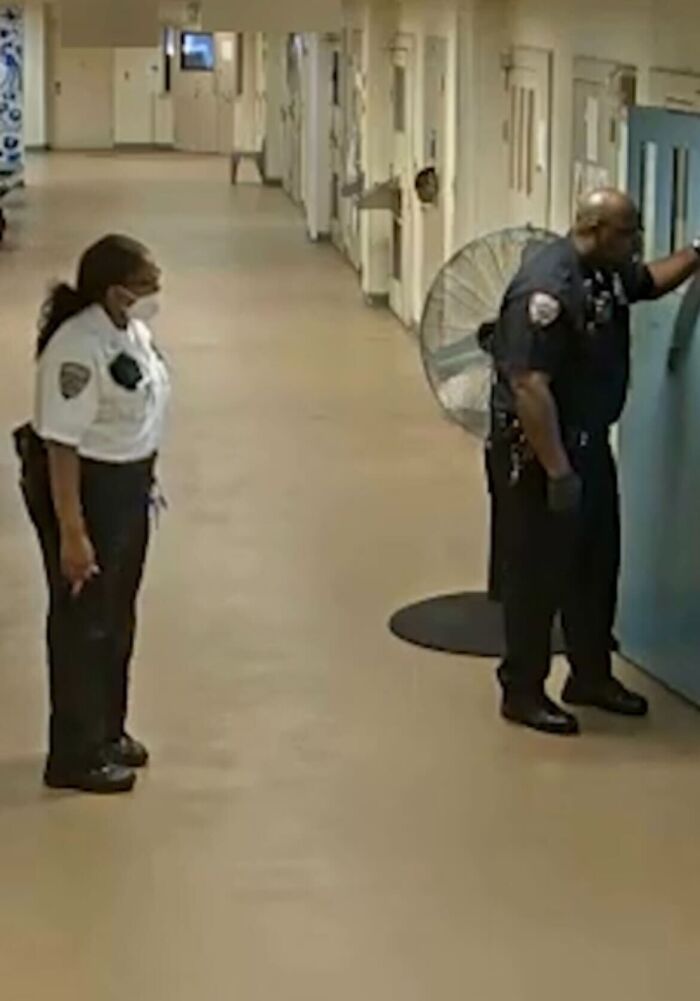 Two correctional officers in uniform stand in a Rikers Island prison hallway, highlighting systemic dysfunction concerns.