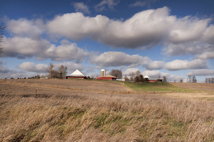 Rural farm landscape with barns and silos under a cloudy sky, related to agriculture and farmworkers.