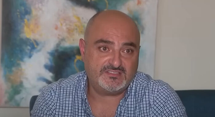 Middle-aged Iranian MAGA supporter in a checkered shirt speaking during an interview in a home setting.