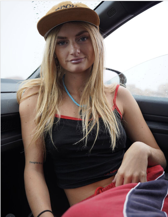 Young woman wearing a brown cap and black tank top sitting in a car, related to NJ police chief abuse allegations.
