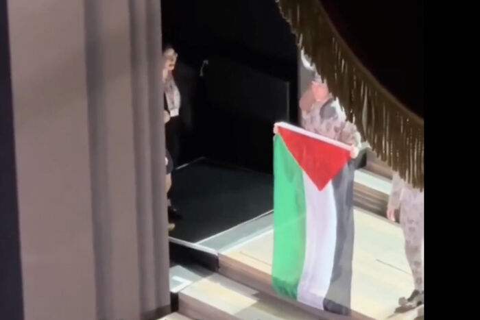 Performer at Royal Opera House holding a Palestinian flag onstage as chaos unfolds during the event.
