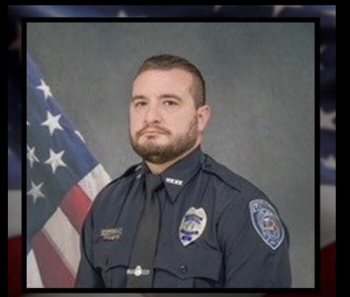 Ohio police officer in uniform posing formally with American flag in background after ambush shooting incident.