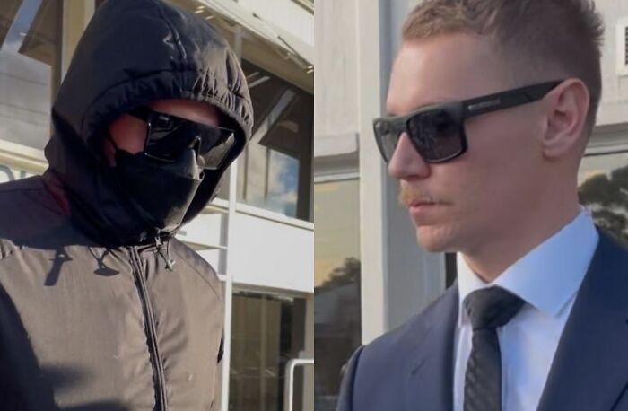Two men wearing dark sunglasses, one in a hooded jacket and the other in a suit, outside a building during daytime.
