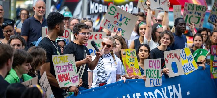 Young climate activists holding signs and speaking at a protest about climate change and international justice cases.
