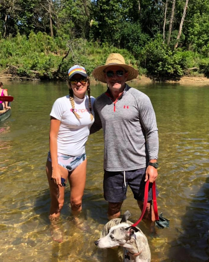 Man and woman standing in shallow river with dog, related to dad leaving soul-crushing voicemails before Texas floods.