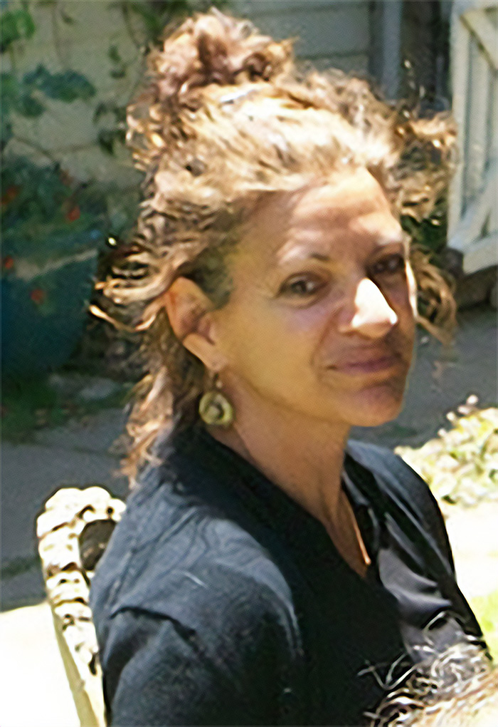 Woman with curly hair sitting outdoors, reflecting as a survivor reacts to Jonestown as new tourist destination.