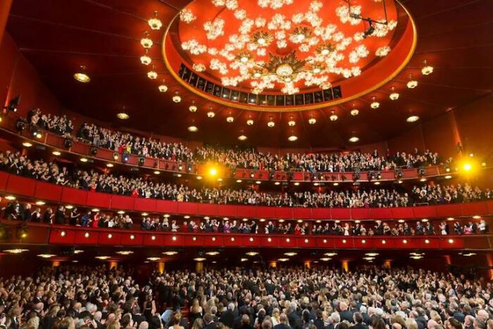 Audience filling the Kennedy Center Opera House with ornate ceiling lights during a formal event or performance.