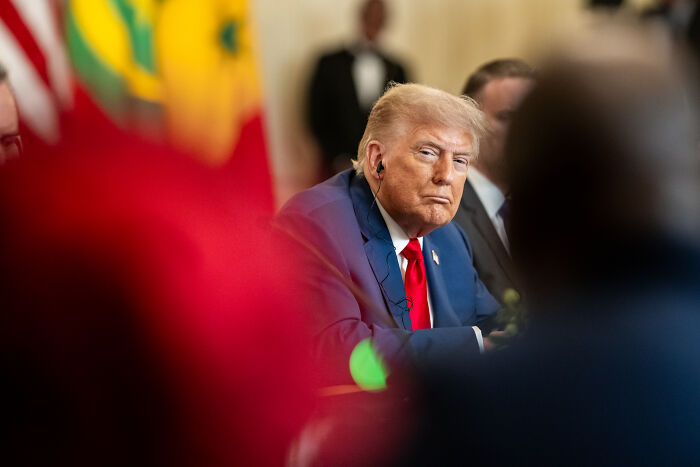 Former president Donald Trump in a suit and red tie attending a meeting, related to Republican lawmaker engagement news.