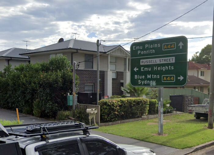 Street signs near residential houses showing directions to Emu Plains, Penrith, and Blue Mountains with a reference to a disturbing officer remark after attack.