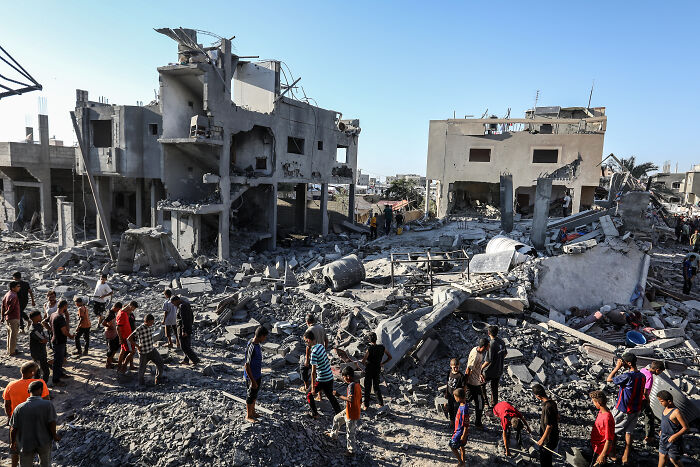 Crowd examines rubble of destroyed buildings in Gaza amid chaos at Royal Opera House after Palestinian flag display onstage.