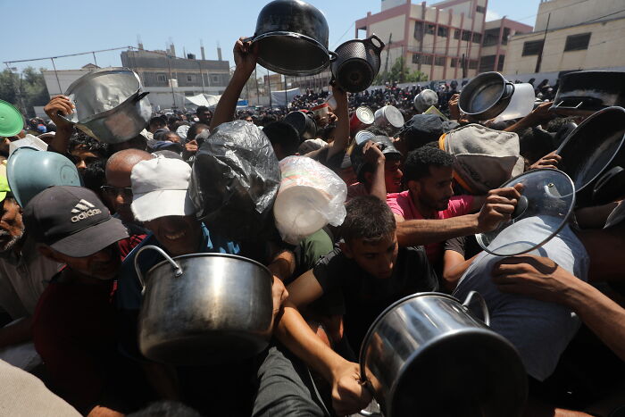 Crowd holding pots and pans during a chaotic protest, highlighting unrest linked to Palestinian flag display at Royal Opera House.
