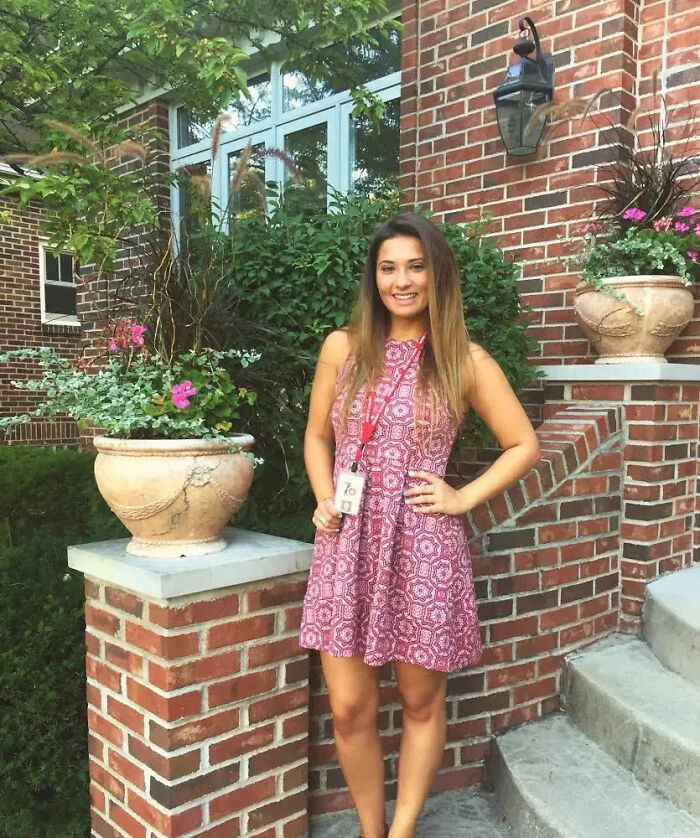 Woman in patterned pink dress standing by brick wall, related to disgraced teacher claims and abuse allegations.