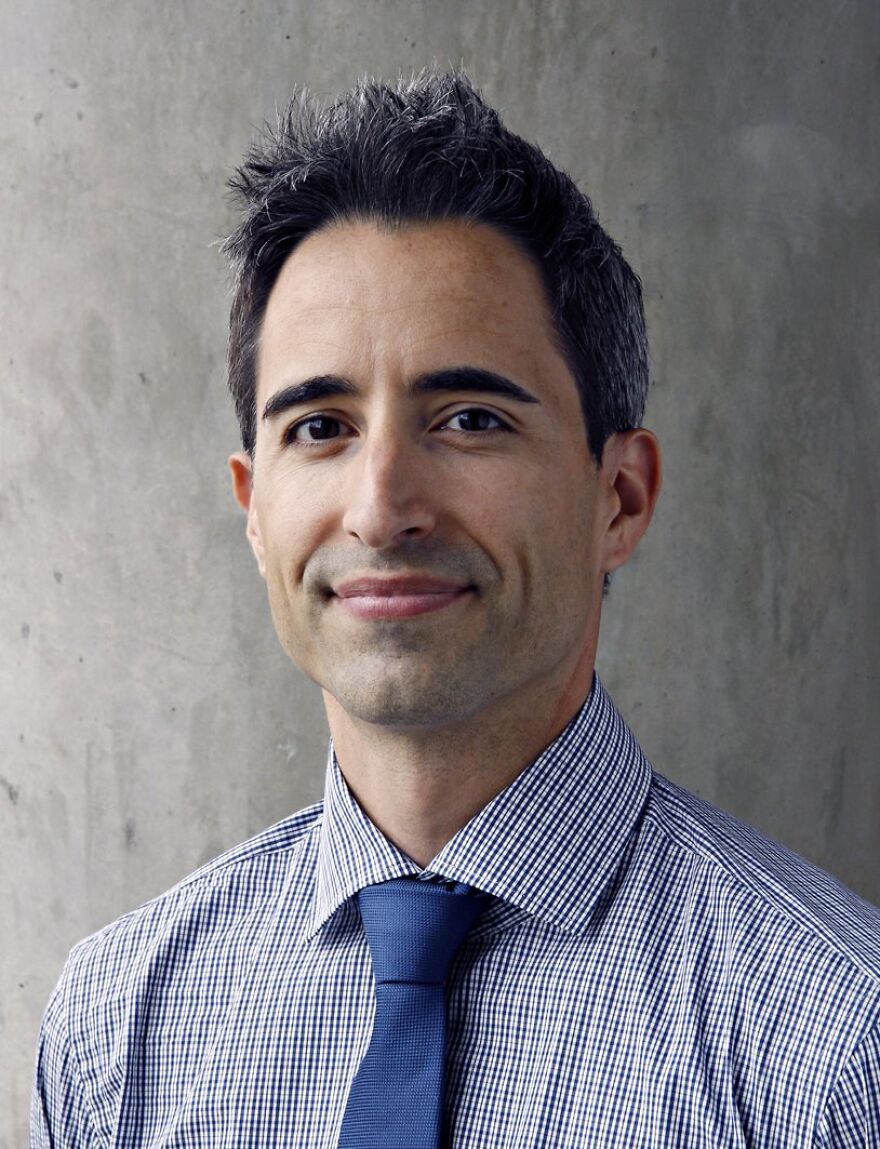 Man in a checked shirt and blue tie posing against a plain wall, representing Alzheimer's research and Big Pharma topics.