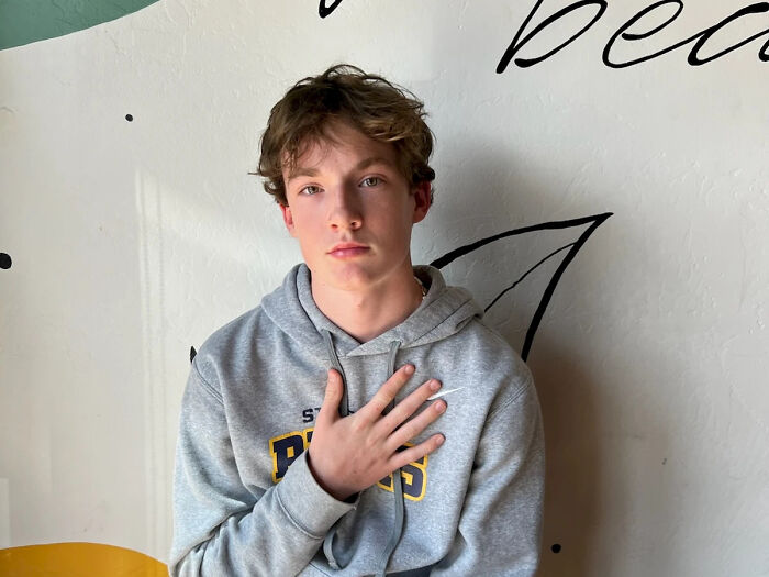 Teen in gray hoodie with hand on chest, illustrating dangers of relying on AI therapists in emotional moments.