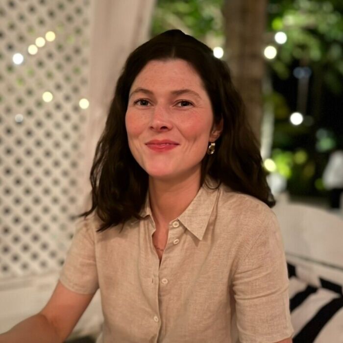 Young woman with dark hair and beige shirt sitting outdoors at night, symbolizing concerns about Uber driver screening lawsuits.