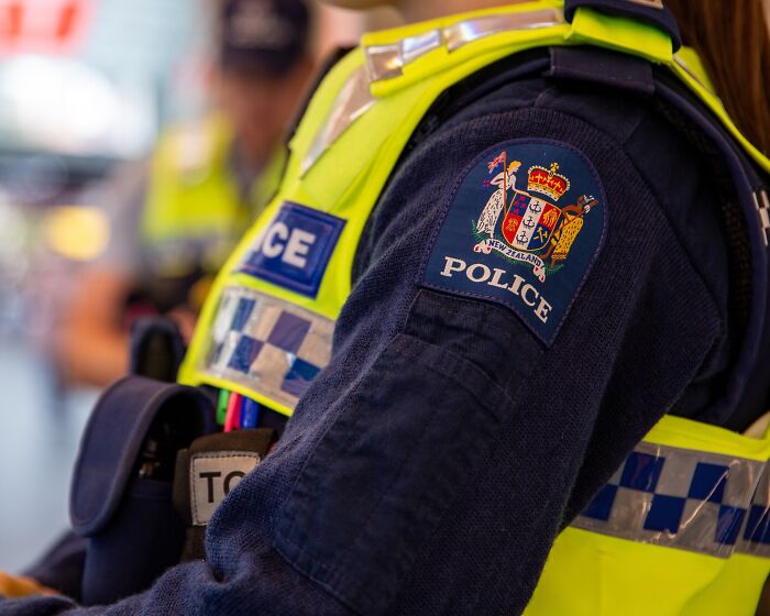 Police officer in reflective vest with New Zealand police patch on arm, related to woman charged with hiding toddler in suitcase case