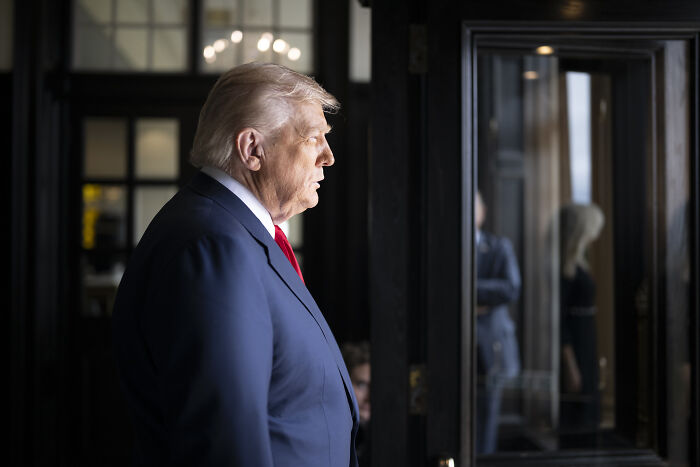 Donald Trump in a suit and red tie speaking indoors during a discussion about the Smithsonian and slavery controversy.