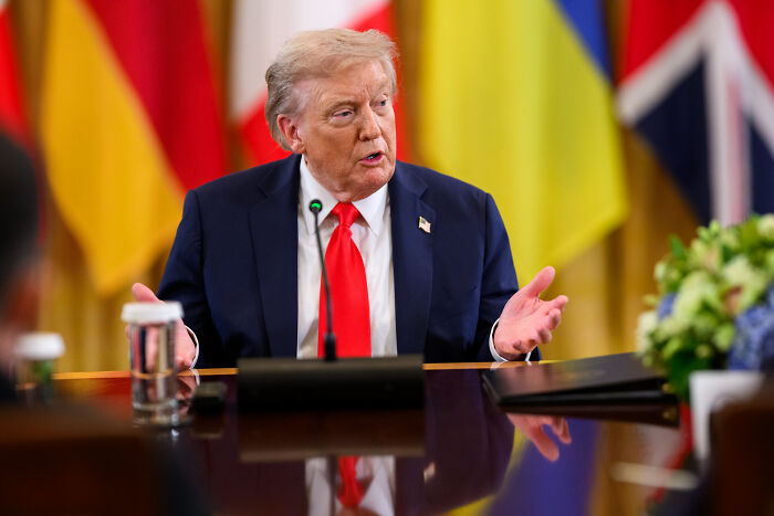Former President Donald Trump speaking at a meeting with flags in the background, unrelated to Gavin Newsom troll game.