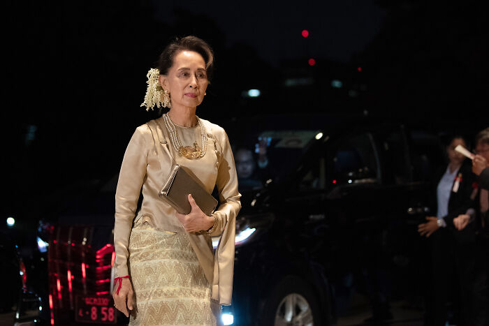 Woman in traditional attire walking at night near a black car, related to Myanmar junta sham election and atrocity allegations.