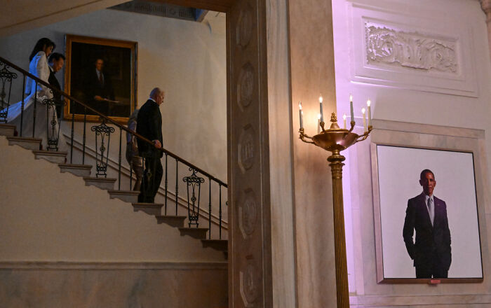 Portrait of Barack Obama displayed in a concealed part of the White House with people walking down nearby stairs.