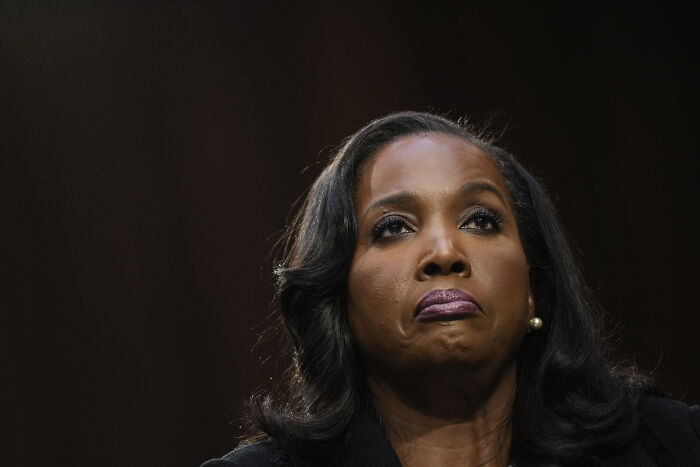 Woman with dark hair and pearl earrings, appearing serious during a formal event related to Fed Chair Jerome Powell investigation.