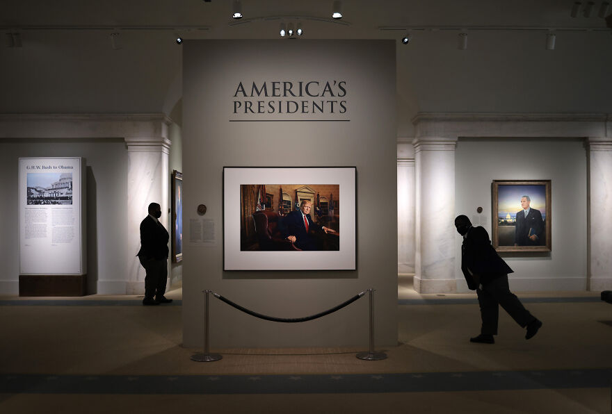 Two visitors in silhouette view presidential portraits in a Smithsonian exhibit amid a sweeping White House review of U.S. history.