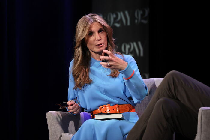 Female MSNBC host speaking during a televised discussion, wearing a blue dress with an orange belt on stage.