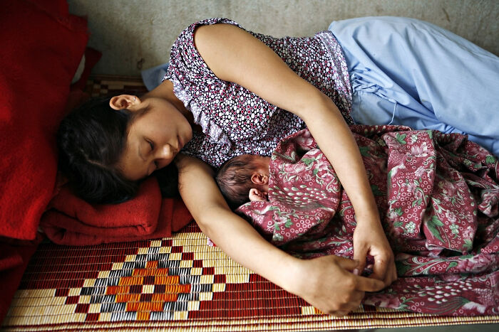 Woman lying on a mat and resting with her newborn baby, illustrating the impact of reproductive rights and health cuts.
