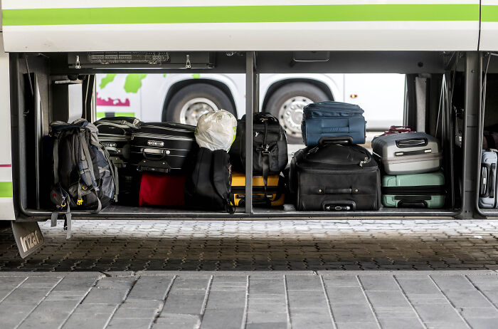Bus luggage compartment open showing various suitcases and bags, related to woman charged for hiding toddler inside suitcase.