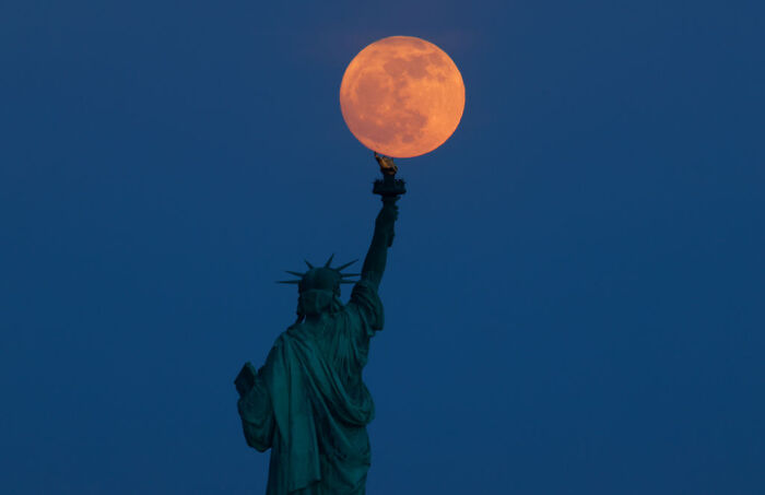 Statue of Liberty holding up a glowing full moon against a clear evening sky symbolizing NASA and the moon reactor plans.