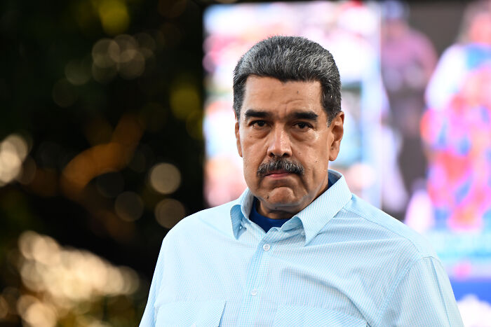 Nicol&aacute;s Maduro wearing a light blue shirt, looking serious outdoors with blurred background and bokeh lights.