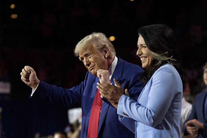 Donald Trump and Tulsi Gabbard smiling and clapping at a public event with focus on intelligence subversion clearances revoked.