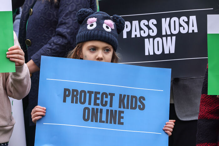 Child holding a sign that says Protect Kids Online at a protest against platforms fueling the child exploitation economy.