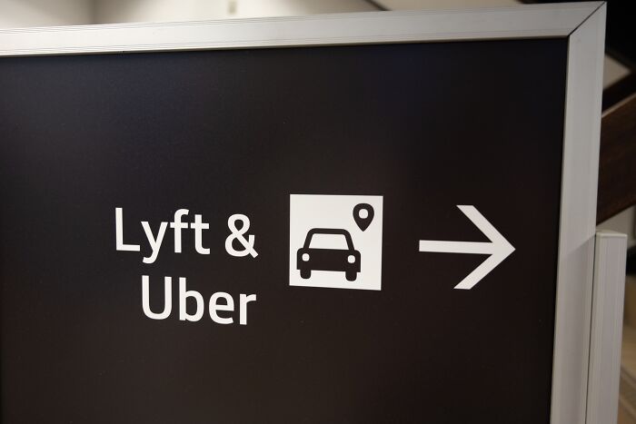Sign directing to Lyft and Uber ride services with car and location icon on a black background highlighting driver screening issues.