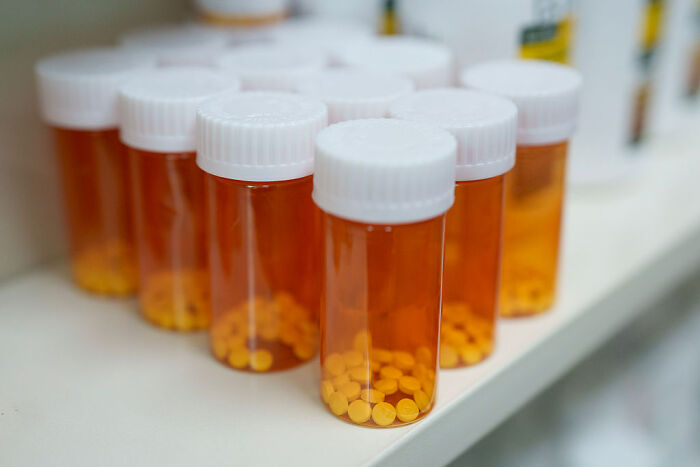 Several prescription pill bottles with white caps filled with yellow tablets, illustrating drug pricing and Big Pharma.