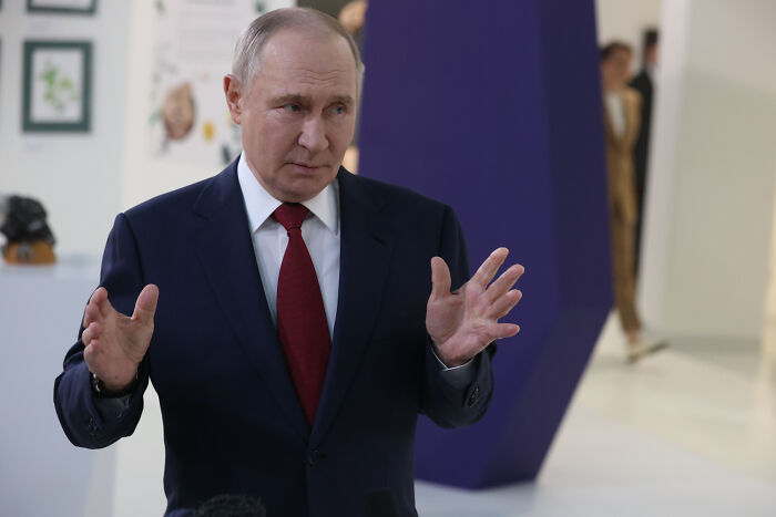 Vladimir Putin in a dark suit and red tie, speaking with hand gestures about West Bank-style occupation of Ukraine.