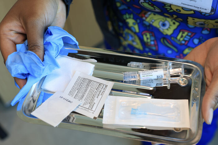 Hands holding a medical tray with syringes and vaccine supplies related to mRNA vaccine development funding.