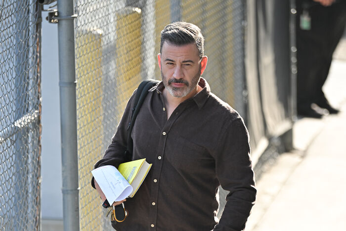 Jimmy Kimmel walking outdoors holding papers, confirming new citizenship amid celebrities leaving the U.S.