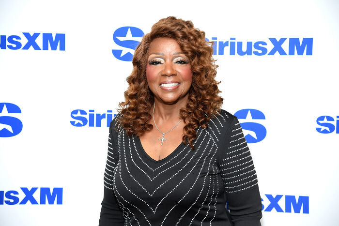 LGBTQ+ icon Gloria Gaynor smiling at SiriusXM event, wearing black top with silver embellishments and curly hair.