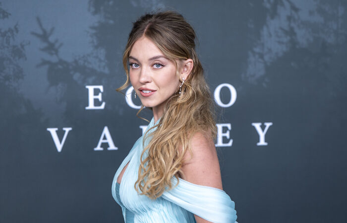 Sydney Sweeney posing at an event, wearing a light blue dress, related to Trump praising controversial jeans advert.