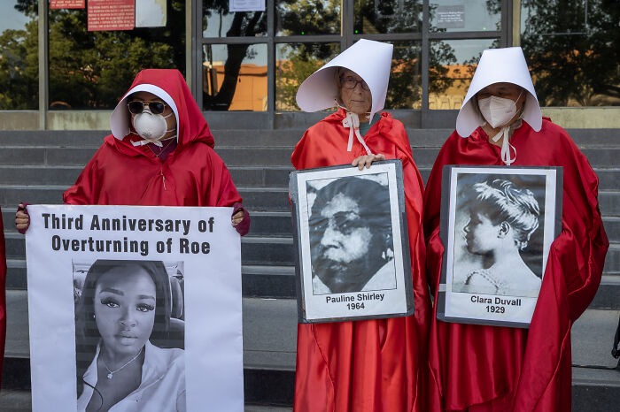 Protesters dressed as handmaids holding signs highlight human rights issues in a U.S. human rights report context.